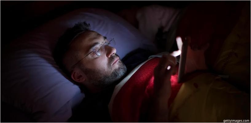 um homem olha para o telefone antes de dormir