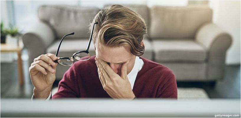 um homem esfrega os olhos na frente de um computador