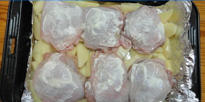 Coxas de frango em um travesseiro de batatas antes de assar em uma assadeira