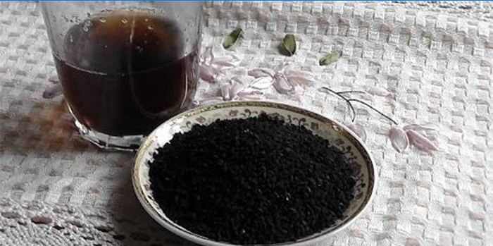 Um copo com infusão e um prato com sementes de cominho preto