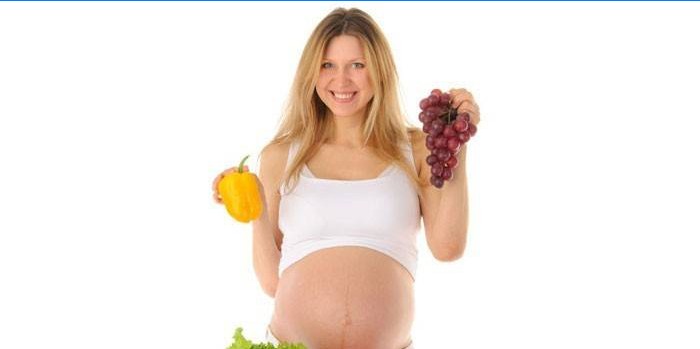 Uma mulher grávida tem pimenta e um cacho de uvas nas mãos