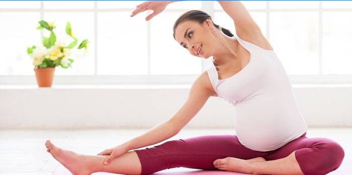 Mulher grávida realiza um exercício enquanto está sentado no chão