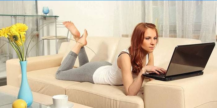 A menina encontra-se em um sofá com um laptop